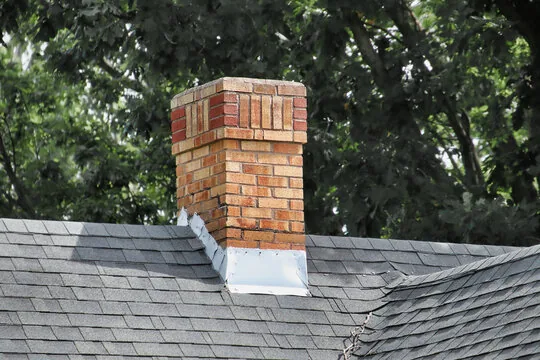 Weathered brick chimney with decorative top courses and metal flashing among dark trees